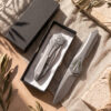 Premium titanium EDC folding knife with Takefu VG10 satin blade shown deployed and closed inside an elegant black gift box with cleaning cloth.